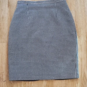 Svartvit rutig kjol från H&M - Snygg svartvit rutig kjol från H&M:s Woman Collection. Kjolen har en klassisk pennkjolssilhuett med en liten slits baktill för extra rörelsefrihet. Perfekt för en stilren look.