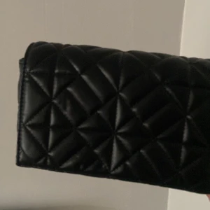 Svart quiltad axelväska med kedja - Snygg svart axelväska med quiltat mönster och en stilren kedja som axelrem. Perfekt för att ge din outfit en elegant touch. Väskan är både praktisk och trendig.