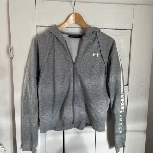 Hoodie från Under Armour - Grå hoodie från Under Armour med detaljer, i storlek M. I bra använd skick!