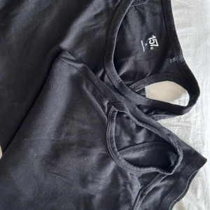 Svarta linnetoppar - Två svarta linnetoppar i enkel design. Perfekta för lager-på-lager eller att bära som de är. Bekväma och mångsidiga för olika tillfällen.