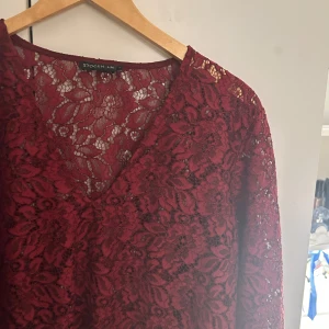 Vinröd spetsblus från Stockh LM - Elegant vinröd spetsblus från Stockh LM med v-ringning och långa ärmar. Perfekt för en stilfull look med sitt vackra spetsmönster.