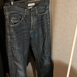 Mörkblå jeans från Stone Island - Snygga mörkblå jeans från Stone Island med klassisk femficksdesign och märkets ikoniska logga på bakfickan. Jeansen har en knappgylf och kontrastsömmar som ger en stilren look.