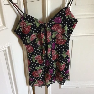 Blommig och prickig linnetopp - Säljer en snygg linnetopp med blommigt och prickigt mönster. Toppen har smala axelband och en knytning framtill. Perfekt för en somrig look!