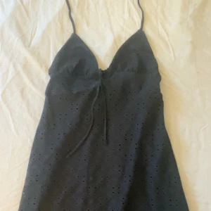 Svart klänning med spetsdetaljer - Snygg svart klänning med smala axelband och spetsdetaljer. Perfekt för en somrig look. Klänningen har en v-ringad design och knytning framtill med öppen rygg! Storlek xs!🥰