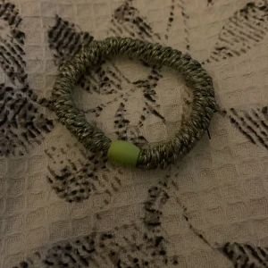 Grönt armband från Kknekki - Säljer ett coolt armband från Kknekki i ljusgrön och silverfärgad ton. Armbandet är elastiskt och har en tvinnad design med en liten grön detalj där märket står. Perfekt accessoar för att ge din outfit lite extra färg.