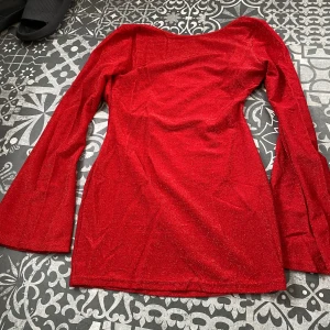 Röd glittrig kortklänning med trumpetärm - Snygg röd kortklänning med glittrigt tyg och långa trumpetärmar. Klänningen har en draperad v-ringning och smala band som knyts i nacken. Aldrig använda bara provad☀️