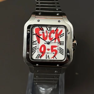 Seiko fyrkantig klocka i stål - Unik Seiko klocka med fyrkantigt boett i borstat stål och matchande länkarmband. Vit urtavla med svarta romerska siffror och coolt röd graffiti-tryck. Automatiskt urverk och blå visare ger en extra touch. Perfekt för dig som vill sticka ut.