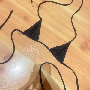 Svart trekantsbikini med knytband - Snygg svart trekantsbikini med tunna knytband som går att justera både i nacken och runt ryggen. Klassisk och stilren modell som passar perfekt till stranden eller poolen. Materialet känns mjukt och följsamt mot huden.