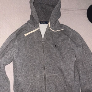 Grå hoodie från Polo Ralph Lauren - Säljer en grå hoodie från Polo Ralph Lauren med dragkedja och huva. 