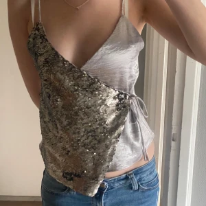 Silver paljettopp från Mango XS - Supersnygg asymmetrisk topp från Mango i silver. Tunn axelbandsmodell med omlott och knyt i sidan. Perfekt festtopp! Är xs men passar snarare som S, även väldigt justerbar då man knyter den.