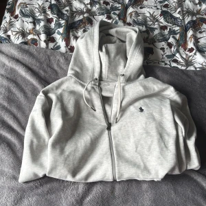 Ljusgrå hoodie från Polo Ralph Lauren - Säljer en stilren ljusgrå hoodie från Polo Ralph Lauren i storlek M. Tröjan har dragkedja, huva med snörning och två fickor framtill. Klassisk broderad logga på bröstet. Perfekt för en chill och avslappnad look. Köpt från zalando för 2300 kr qr kod funkar, kommer dirket till zalando och där tröjan köptes länken.