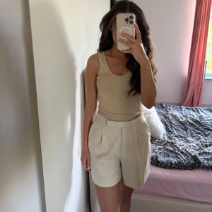 Beiga glittriga shorts från Zara - Snygga beiga shorts från Zara med diskret glittrig effekt. De är högmidjade med bred linning och har en klassisk, lite lös passform. Perfekta för dig som vill ha en stilren men ändå extra look. Stängs med dold dragkedja framtill.