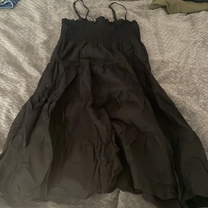 Svart sommarklänning med smock - Svart långklänning från Divided med smala axelband och smockad överdel. Klänningen har en luftig och flowy kjol, perfekt för varma dagar. Enkel och stilren design som passar till många tillfällen.