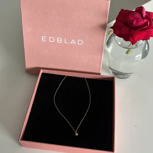 Guldigt halsband från Edblad - Stilrent halsband från Edblad i guldton med tunn kedja och en liten rund kula som hänge. Perfekt för dig som gillar minimalistiska smycken med en elegant touch. Levereras i original ask.