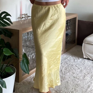 Ljusgul långkjol satin - Snygg ljusgul långkjol och glansigt satintyg. Kjolen har en enkel midjeresår. Perfekt att matcha med en gul satintop eller en oversize skjorta/tshirt i sommar. Ursäkta att jag ej strukit den.