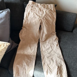 Beiga cargopants från Gina Tricot - Säljer ett par beiga cargopants från Gina Tricot i storlek 34. Byxorna har flera fickor på sidorna och bak, elastisk midja och är tillverkade i ett lätt bomullsmaterial. Perfekta för en avslappnad och trendig look.