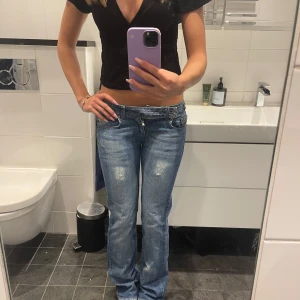Lågmidjade bootcut jeans i ljusblå denim - Säljer ett par snygga lågmidjade bootcut jeans i ljusblå denim med slitningar framtill och bakfickor. Jeansen har klassisk femficksdesign, dragkedja och knappstängning. Perfekta för dig som gillar en avslappnad och trendig look.