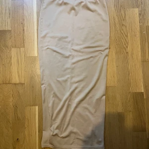 Beige långkjol med slits - Snygg beige långkjol i enkel och stilren design. Kjolen har en rak passform och en slits baktill. Perfekt att matcha med en crop top eller oversized tröja för en chill look.