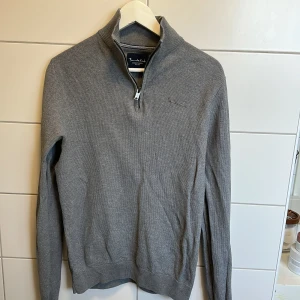 Grå stickad half zip från Bondelid - Snygg grå stickad tröja från Bondelid med halv dragkedja och hög krage. Tröjan har diskret broderad logga på bröstet och ribbade muddar. Perfekt för lager-på-lager och chill stil under höst och vinter. Priset är inte hugget i sten! 