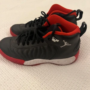 Svarta Air Jordan sneakers strl 39 - Snygga svarta Nike Air Jordan sneakers med röda och vita detaljer. Skorna har klassisk Jumpman-logga, svart snörning och röd insida. Ovandelen är i skinn och sulan har coolt mönster i rött, vitt och svart. Perfekta för dig som vill sticka ut med en ikonisk streetstil.