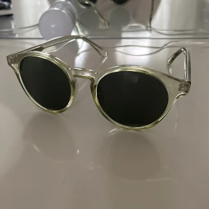 Runda  solglasögon - Snygga solglasögon med rund form och transparent plastbåge. Glasen är mörka och ger en cool kontrast mot den ljusa ramen. Perfekt accessoar för att lyfta din stil under soliga dagar.