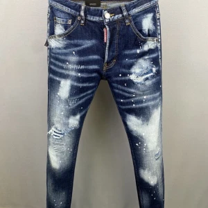 Dsquared2 Bella Ciao Jeans - Mörkblå skinny jeans från Dsquared2 med coolt blekta partier, slitningar och vita färgstänk. Bakfickan har handskriven graffiti-text för extra edge. Klassisk femficksmodell med gylf och knapp, samt kontrastsömmar. Perfekta för dig som gillar streetstyle.