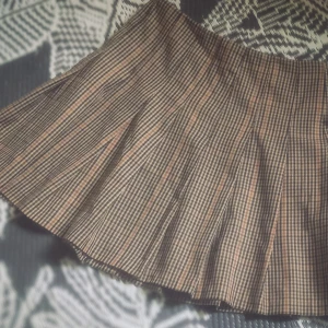 Rutig plisserad kortkjol i brunt - Superfin kortkjol med rutigt mönster i bruna och beige toner. Kjolen är plisserad och har en klassisk skoluniform-vibe. Perfekt för dig som gillar preppy stil och vill sticka ut lite extra. Materialet känns som bomull eller polyester.