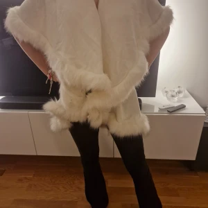 Vit pälsväst med fluffiga kanter - Säljer en superfin vit pälsväst med breda, fluffiga kanter i fuskpäls. Västen har en lös och oversized passform och är perfekt för att ge din outfit en lyxig touch. Den är ärmlös och har en mjuk, mysig känsla som sticker ut.