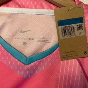 FC Barcelona rosa matchtröja Nike M - Säljer en helt ny FC Barcelona fotbollströja från Nike i storlek M. Tröjan är rosa med ljusblå detaljer, har klubbmärke och Nike-logga på bröstet samt Spotify-logga i svart. Tillverkad i lätt, ventilerande Dri-Fit-material och har korta ärmar. Perfekt för dig som älskar Barca och vill sticka ut. Aldrig använt nypris 1200 