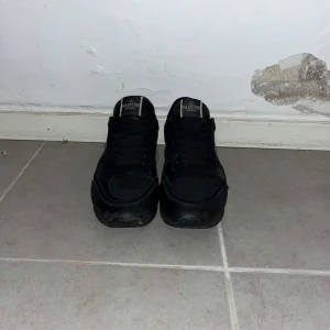 Svarta Valentino Rockrunner sneakers - Snygga helsvarta Valentino Rockrunner sneakers med coola nitar på hälen och klassisk logga på plösen. Skorna har snörning, rund tå och är tillverkade i en mix av skinn och mocka för en lyxig känsla. Perfekta för dig som gillar stilrena och exklusiva sneakers.