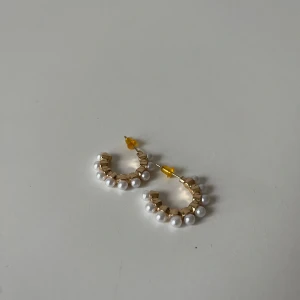 Guldiga örhängen med pärlor - Snygga örhängen i guldtonad metall med vita pärlor längs hela bågen. 