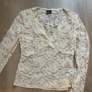 Beige spetsblus från Gina Tricot - Supersnygg beige spetsblus från Gina Tricot i storlek XS. Blusen har lång ärm, v-ringning och är helt täckt av blommig spets. Perfekt för dig som gillar romantiska detaljer och vill sticka ut lite extra.