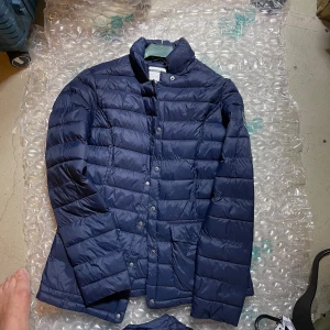 Mörkblå dunjacka från Race Marine - Snygg mörkblå dunjacka från Race Marine med klassisk quiltad design och hög krage. Jackan har tryckknappar framtill och en tydlig logga på ärmen. Perfekt för kyliga dagar och enkel att matcha med olika outfits.