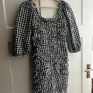 Rutig kortklänning från Bik Bok - Supersöt svartvit rutig kortklänning från Bik Bok med puffiga trekvartsärmar och smockad rygg. Klänningen har rynkade detaljer framtill och är gjord i mjuk bomull. Perfekt för dig som gillar en trendig och lekfull stil.