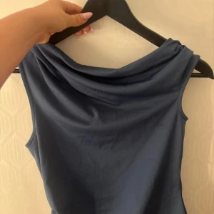 Mörkblå ärmlös linnetopp - Snygg mörkblå ärmlös linnetopp med draperad halsringning. Toppens enkla och stilrena design gör den lätt att matcha med olika outfits. Mjuk och följsam känsla i materialet, perfekt för varmare dagar. Nypris 300kr aldrig använd