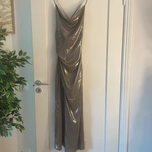 Glittrig långklänning med snörning - Supersnygg långklänning i blank sliver/guld med tunna axelband och draperad framsida. Klänningen har snörning i ryggen och en slits framtill. Köpte på Adoore Outlet för något år sedan men bara provat någon gång annars helt ny. Passade inte mig och inte min stil men annars jätte snygg och perfekt till en utekväll🥂💕