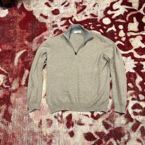 Beige half zip tröja Gran Sasso - Stilren beige tröja från Gran Sasso med halv dragkedja och hög krage i kontrasterande grått. Tröjan är stickad och har långa ärmar samt ribbade muddar. Perfekt för lager-på-lager och snygg till jeans eller chinos. Ett litet hål i vänster arm  som ni ser på bild 3, orginalpris 2499kr
