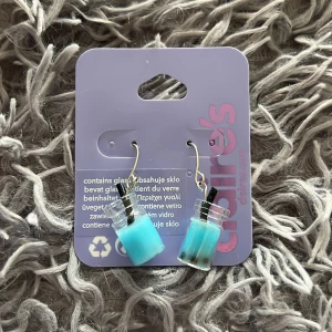 Claire's örhängen med blå bubbelte - Superunika örhängen från Claire's formade som små glasflaskor fyllda med blå vätska och svart sugrörsdetalj. Hängande modell som verkligen sticker ut och ger en lekfull vibe till din stil. Perfekta för dig som gillar roliga accessoarer!