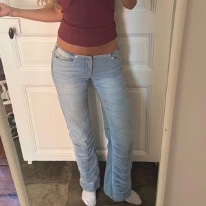 Ljusblå bootcut jeans med mesh tyg - Säljer ett par ljusblå jeans med bootcut-modell och mesh rynkade detaljer längs hela benen. Jeansen har låg midja och klassisk femficksdesign. Innerbenslängden: 80cm. Midja rakt över: 37cm☺️