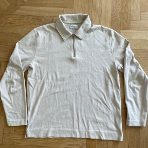 Beige half zip pikétröja These Glory Days - Stilren beige pikétröja från These Glory Days i bomull. Tröjan har lång ärm, klassisk krage och en snygg half zip-dragkedja framtill. Perfekt för dig som gillar en clean och avslappnad look.