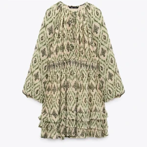 grön klänning  - Supersöt kortklänning med grönt och beige mönster, vida långa ärmar och smock i midjan. Klänningen har volangdetaljer nertill och en avslappnad passform. Perfekt för dig som gillar boho-vibes och unika prints. aldrig använd 