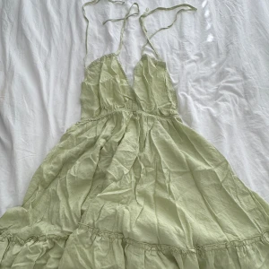 Ljusgrön omlottklänning med volang - Supersöt ljusgrön klänning med tunna axelband som knyts i nacken. Klänningen har omlottkänsla, v-ringning och volangdetaljer nertill. Perfekt flowy passform och lätt material, perfekt för varma dagar.