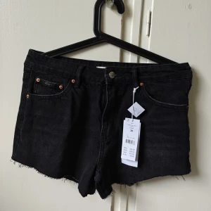 Svarta jeansshorts från Gina Tricot  - Snygga svarta jeansshorts från Gina Tricot i modell med fransig kant nertill. Klassisk femficksdesign, knapp och dragkedja framtill samt bälteshällor. Perfekta till sommaren för en avslappnad och cool look. Ny med prislapp.