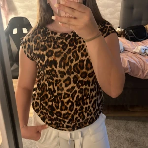 Leopardmönstrad topp med kort ärm - Snygg topp med leopardmönster i bruna och svarta toner. Modellen har rund halsringning och korta ärmar, perfekt för dig som vill sticka ut med en djurisk vibe. Tunt och mjukt material som känns skönt mot huden.