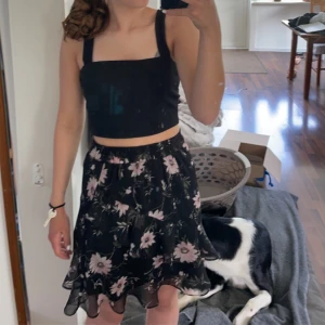 Svart blommig volangkjol - Supersöt svart kjol med rosa blommor och volangkant. Kjolen är hög midjad men går att vika ner. Kjolen är i ett fint skick. Kjolen slutar en liten bit över knäna. Jag skulle säga att det är storlek S men vet inte riktigt då lappen inte finns kvar. 