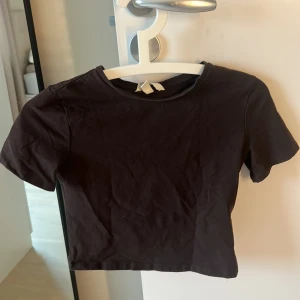 Mörkbrun croppad topp från H&M - En enkel brun croppad topp från H&M med rund halsringning och korta ärmar. Tillverkad i mjuk bomull som känns skön mot huden.