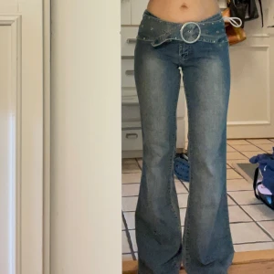 Blå bootcut jeans med snörning - Ett par blå bootcut jeans med låg midja och snygga vita snörningsdetaljer bak i midjan. Jeansen har som ett inbyggt skärp, inga bakfickor och coola detaljer. Säljer då de inte är min stil💔står storlek 7/8 men passar mig som har s. Lite slitna nertill då personen som haft dem innan troligtvis har varit lite för kort för dem, men det går enkelt att vika upp så det inte syns. Innerbenslängd: ca 83 cm. Midjemått: 37 cm rakt över