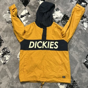 Gul och marinblå vindjacka från Dickies - Säljer en snygg gul och marinblå vindjacka från Dickies med stor logga över bröstet. Jackan har huva, dragkedja upptill och praktiska fickor. Perfekt för dig som gillar streetwear och vill sticka ut med färg. Justerbar nederkant med snörning. Anledning att jag vill sälja är att den är för small på mig nu! 