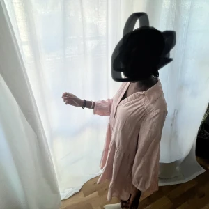 Ljusrosa kort klänning från Zara - Supersöt ljusrosa klänning från Zara med v-ringning och knappar framtill. Klänningen har långa ärmar med lätt puff och är tillverkad i ett luftigt bomullstyg. Den har en avslappnad passform och volangdetaljer nedtill för en extra flowy känsla.