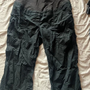 Svarta cargopants med mudd - Gravid byxor /Svarta cargopants med bred mudd upptill, perfekta för dig som vill ha bekväma och funktionella gravid byxor. Stora fickor på sidorna och bakfickor med knapp. Tillverkade i mjukt bomullstyg, loose fit och avslappnad stil. Perfekt om du är gravid / pris kan diskuteras finns även en reserv knapp på lappen 